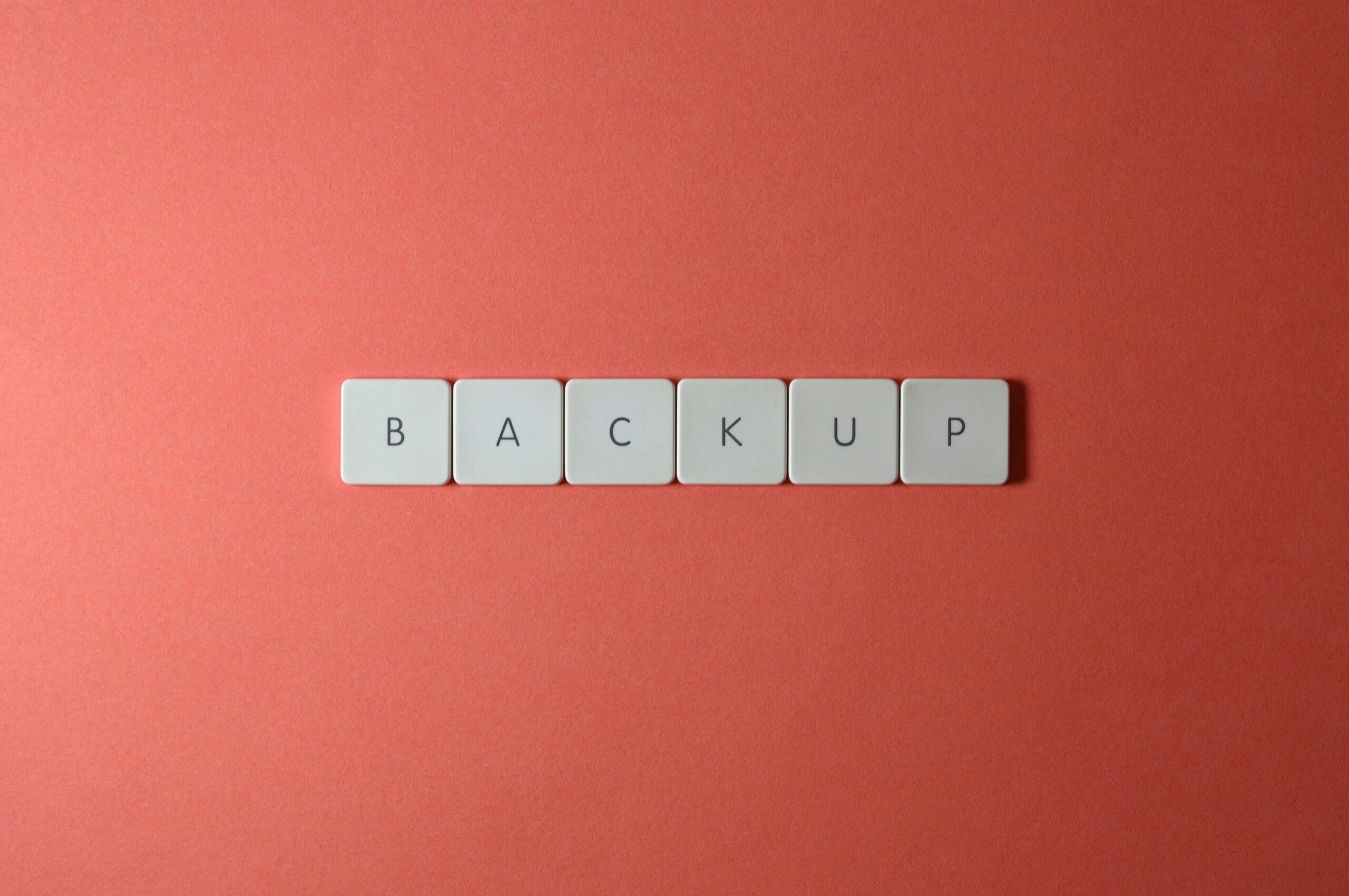 Simple-Backup-and-Recovery-Plans-Every-Small-Business-Needs-scaledjpg Free Close-up of keyboard keys spelling 'BACKUP' placed on a coral-colored surface. Stock Photo